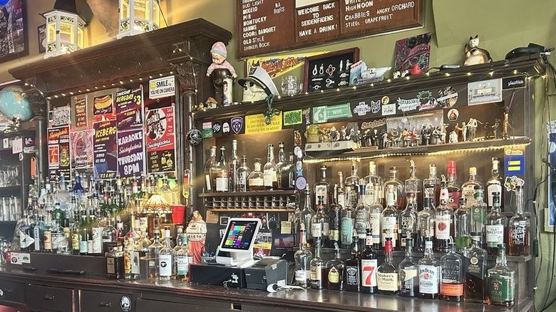 A back bar lined with rows of booze bottles and random objects like figurines, a skull wearing a captain hat, and a cat figurine