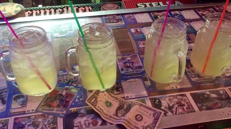 Four margaritas on the rocks in mason jar-style mugs lined up on a bar top that is decorated with football cards