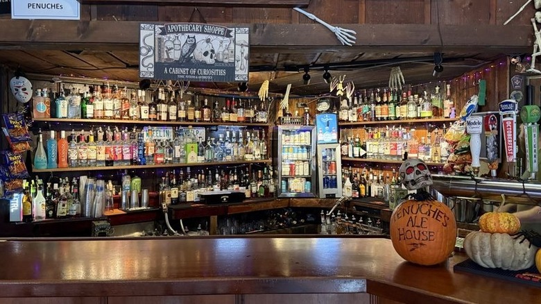 The interior of a bar, decorated for Halloween, showing the back bar with three shelves of liquor bottles against a wood backdrop