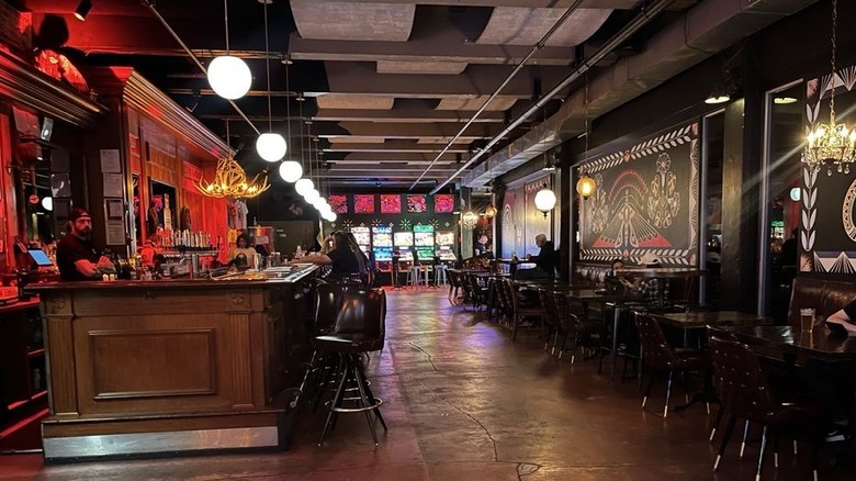 The interior of a dimly-lit bar with a wood bar on the left