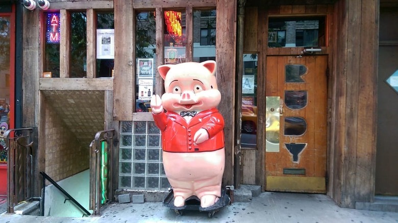 The wooden exterior of Rudy's Bar with a giant porcelain pig statue in front and the wood door has windows carved that spell "Rudy"