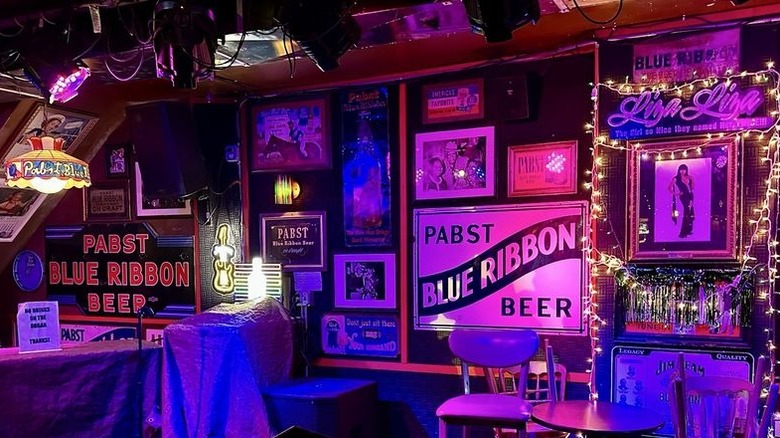 The interior of a dimly-lit bar wall that is densely decorated with PRB memorabilia and white string lights