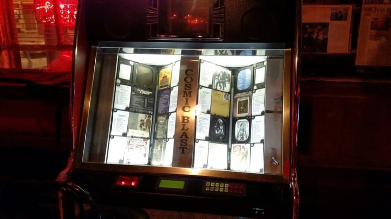 A Cosmic Blast jukebox glowing in a dark room lit by a red neon sign