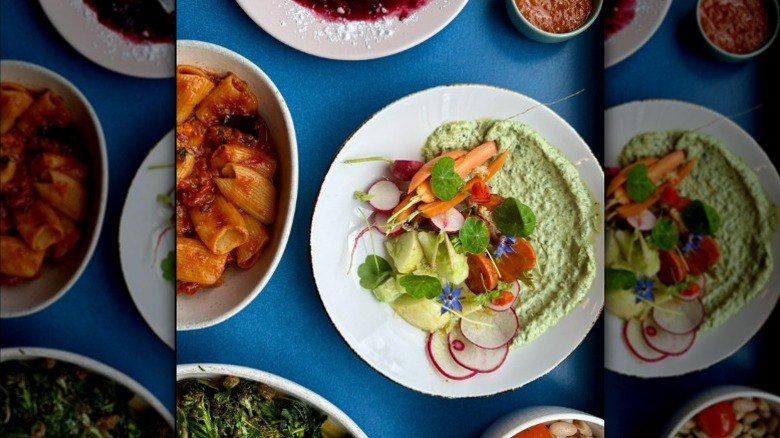 Dishes with vegetables, pasta, and sauces resting on a blue table from Somebody People in Denver, Colorado