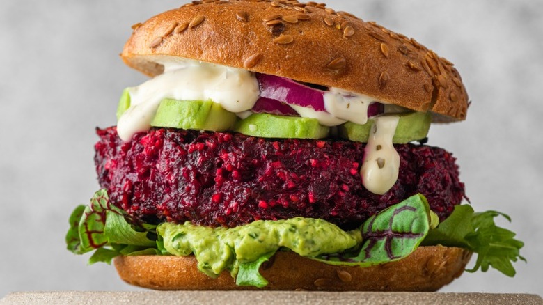 Vegetarian burger with beet patty, lettuce, avocado, onions, and sauce on a seeded bun