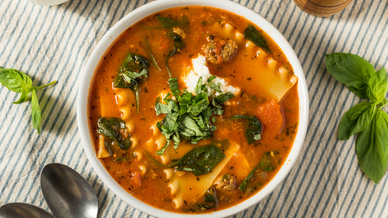 A bowl of ravioli soup topped with fresh herbs on striped linen