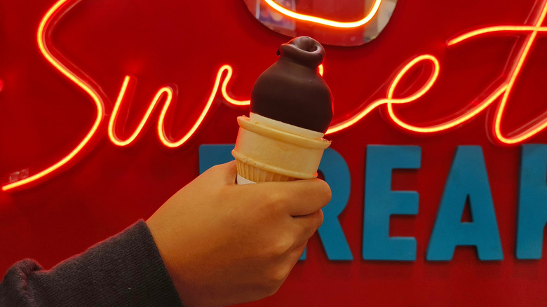Hand holding chocolate dipped cone in front of neon Dairy Queen sign