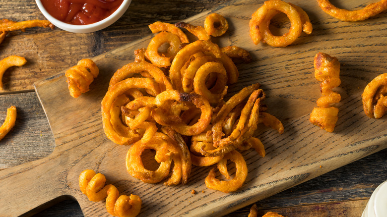 Curly fries on a cutting board with ketchup