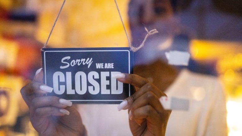 Woman puts up "closed" sign at restaurant door.