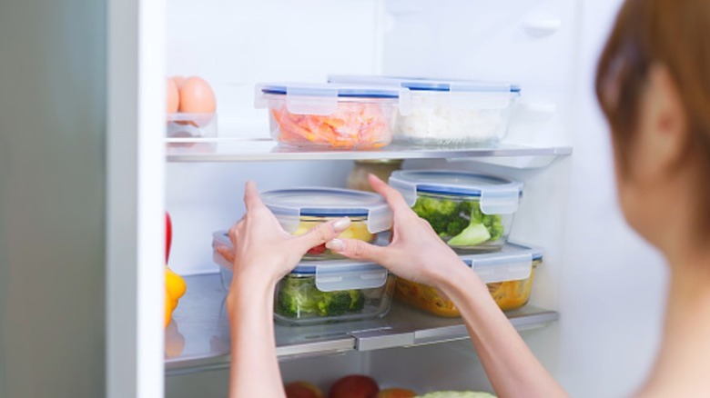 A woman carefully stocking her refrigerator with Tupperware.