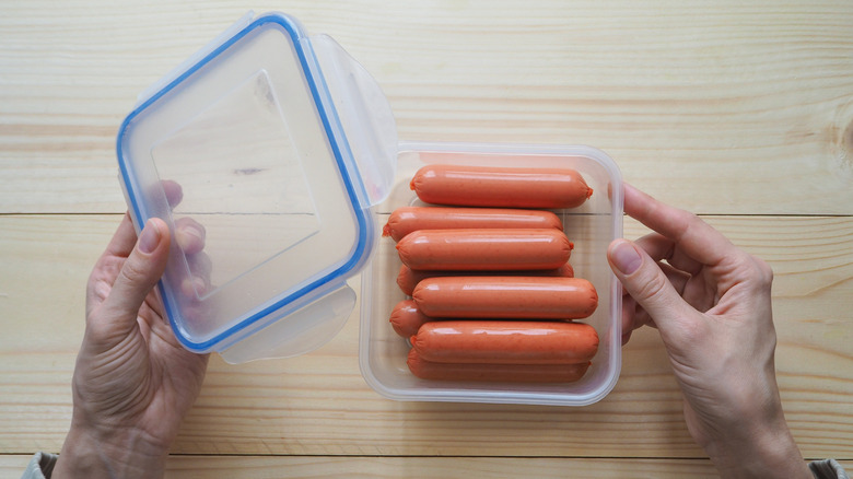 Top view of hands putting a lid on a plastic container of hot dogs