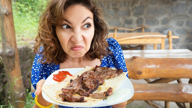 Woman sniffs a spoiled steak and makes a face