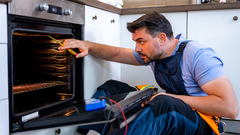A technician working on an oven in a kitchen.