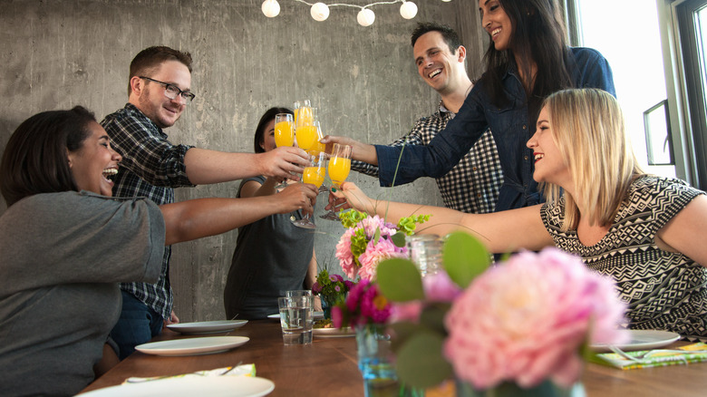A group of friends smiling while cheers-ing their mimosas