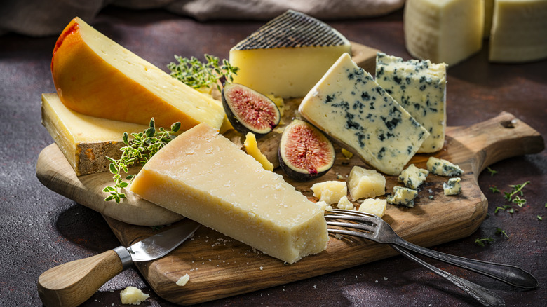 Different cheeses on a board with a sliced fig and some herbs