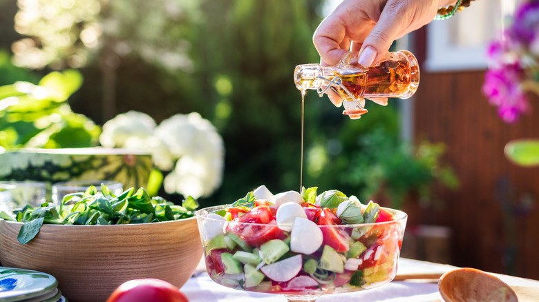 Woman pouring dressing onto a salad set out for a party.