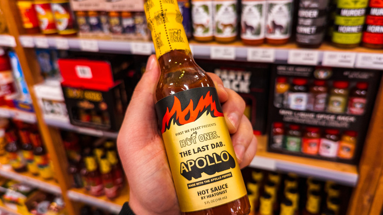 A person holds a jar of Apollo hot sauce by Heatonist in a grocery aisle