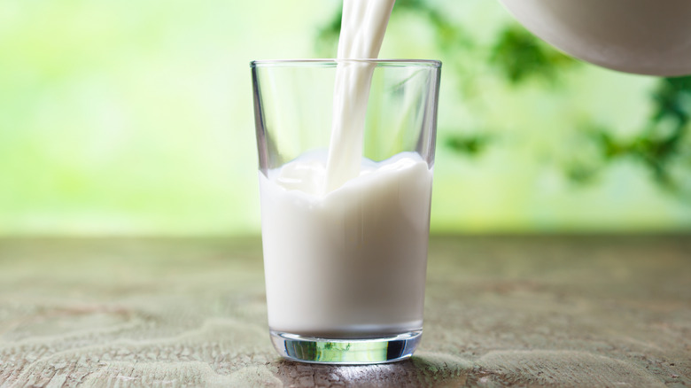 Milk is being poured into a glass which sits on a table