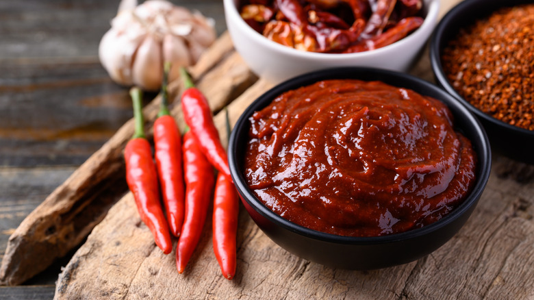 Hot chili peppers rest on a wooden board, along side a bowl of chilli paste