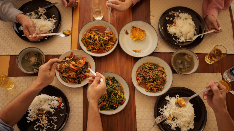 A family is dining together at a wooden table adorned with various dishes, including rice, green beans, and shrimp