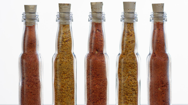 Five glass bottles with stoppers in a row of different hot chili pepper flakes