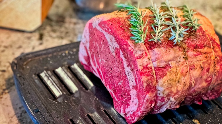 Raw seasoned prime rib with rosemary sprigs on top