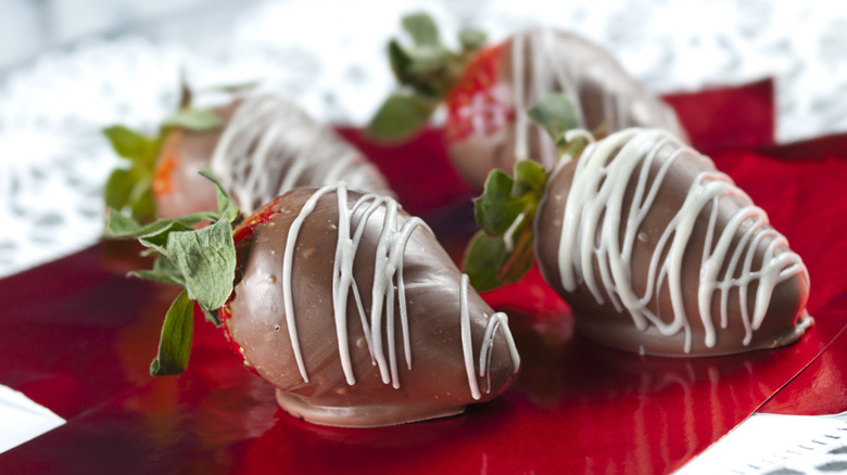 Four chocolate-covered strawberries are shown with white chocolate drizzle