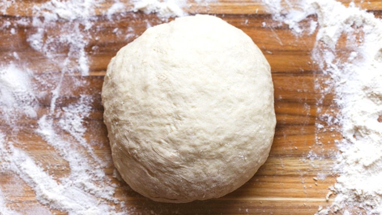 A ball of bread dough on a wooden board with flour