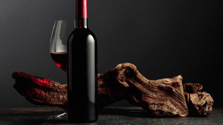 A bottle of red wine without a label in front of a glass of wine