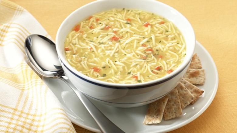 Chicken noodle soup in a white bowl next to a spoon
