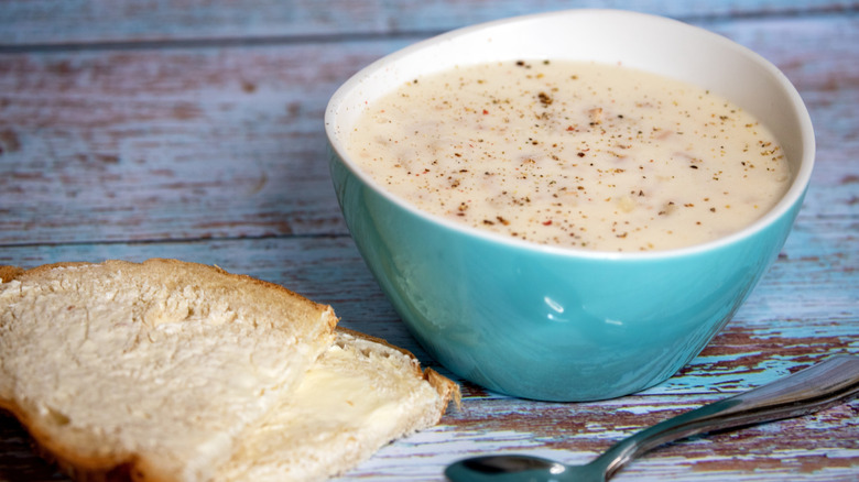 Clam chowder in a blue bowl next to a piece of bread