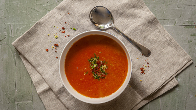Tomato soup in a white bowl next to a spoon