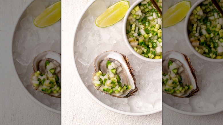 An oyster in a half shell on ice next to a cucumber mignonette sauce with a lime wedge