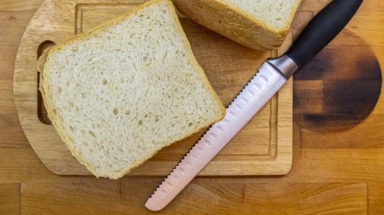 Serrated knife with white bread on a wooden cutting board.