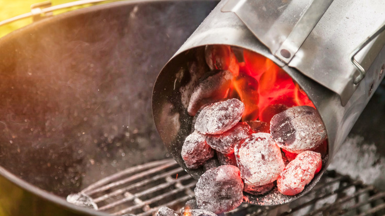 Hot charcoal briquettes being poured from a chimney starter onto a grill.