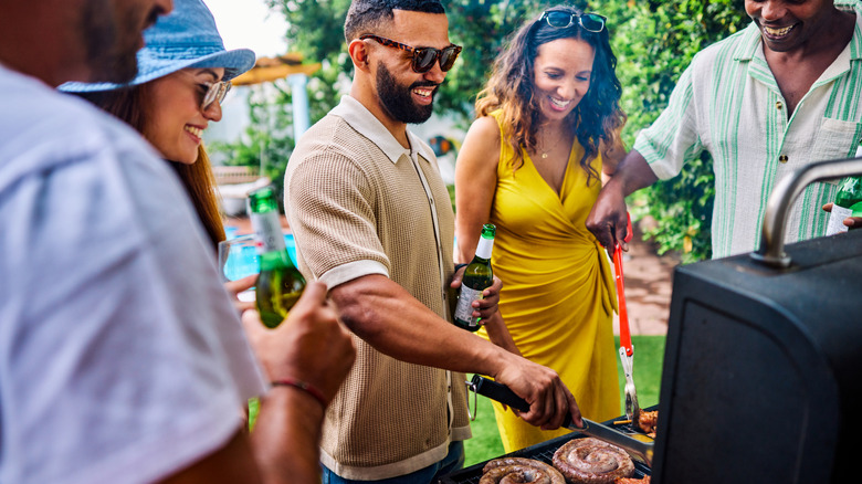 Group of people standing around a grill at a cookout