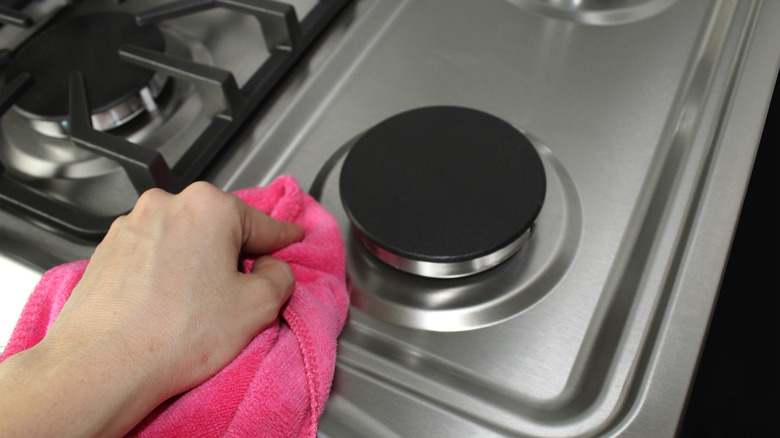 A person's hand with a pink microfiber cloth cleaning a gas stovetop.