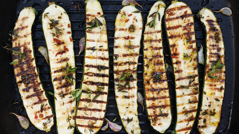 zucchini halves on the grill with grill marks showing and sprinkled with herbs