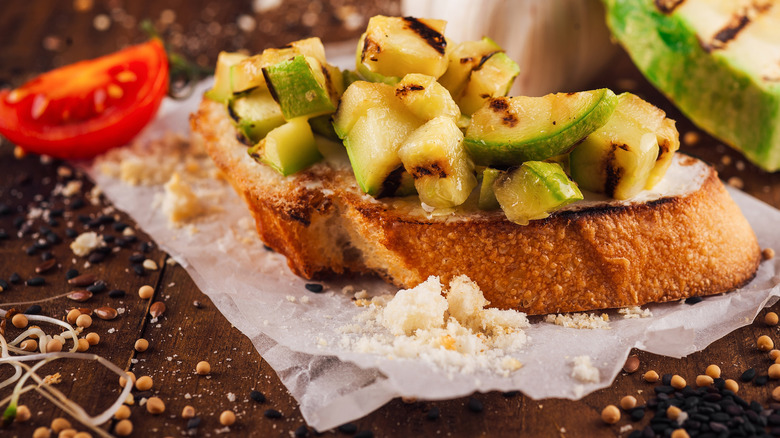 Chopped grilled zucchini on top of toasted bread bread slice