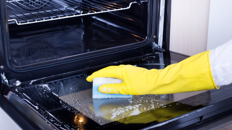 Hand in yellow glove cleaning the inside of a glass oven door
