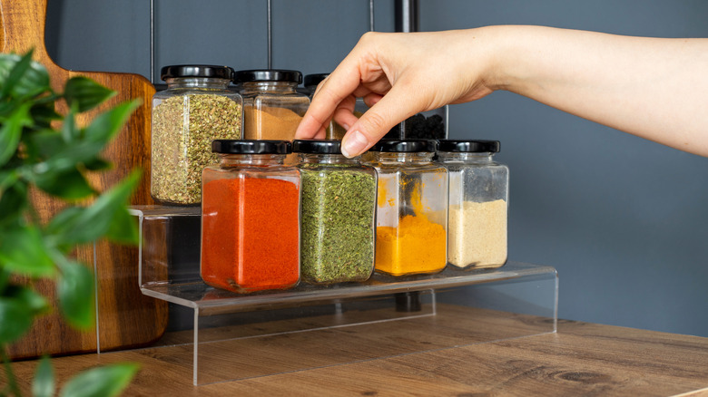 A person picking spices from a shelf.