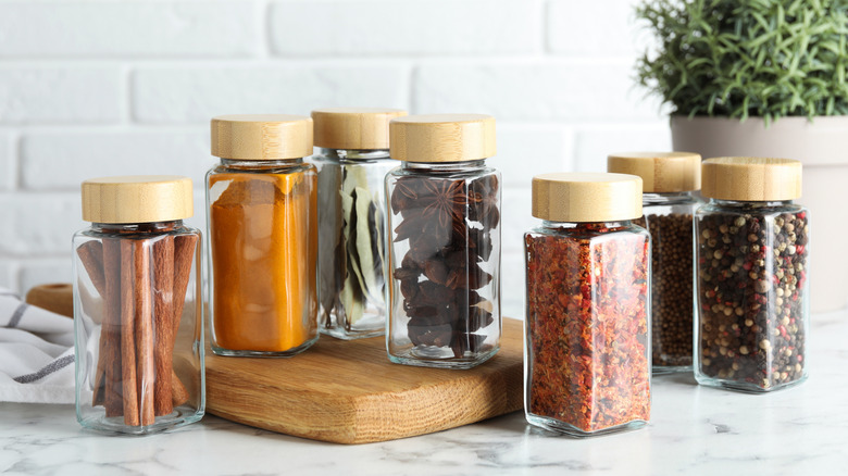 Several small glass jars sitting on a marble surface and wooden cutting board.