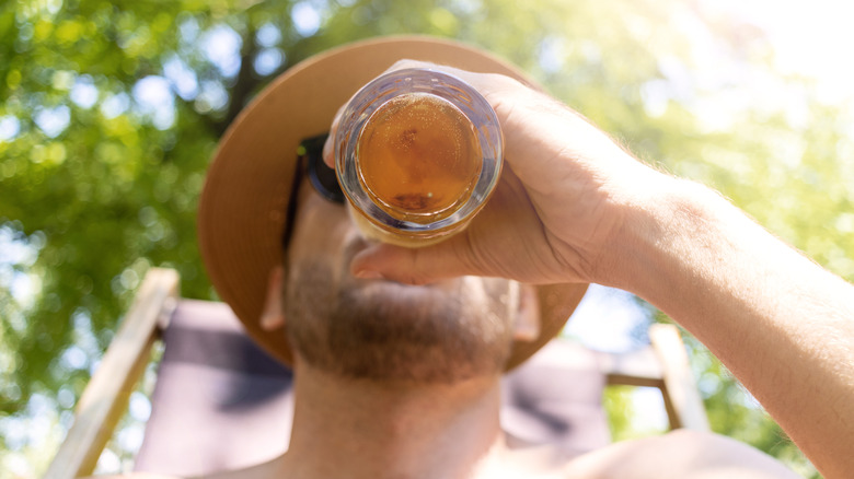 The view from the bottom of the glass as a man drinks a beer outside on a sunny day