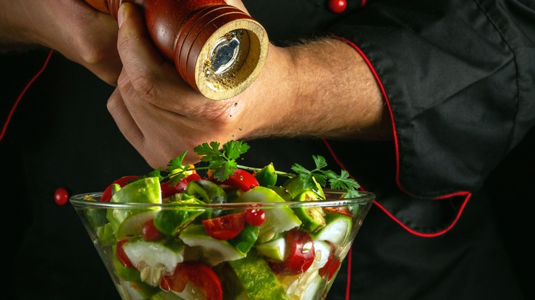 A chef grinds pepper onto a vegetable salad