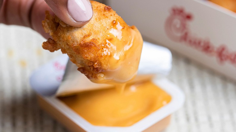 Fingers dipping chicken nugget into Chick-fil-A sauce