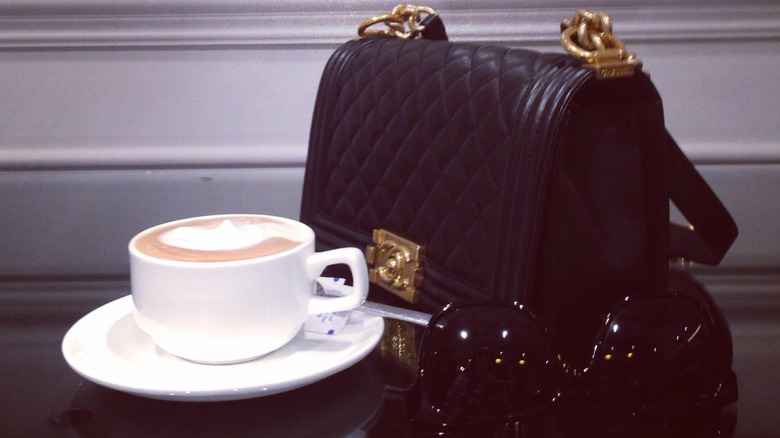 A Chanel purse on a table top with a cup of coffee and a pair of sunglasses in the forefront