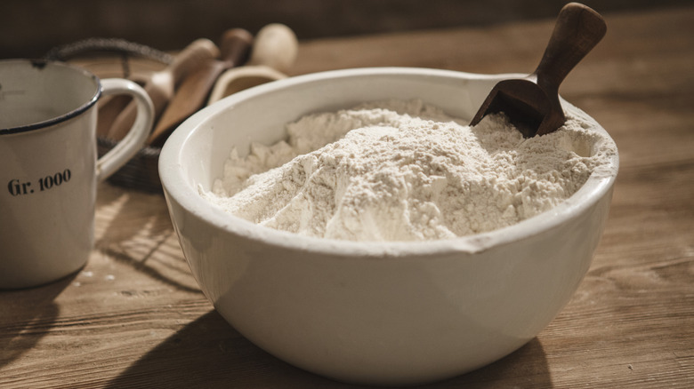 A bowl of white flour with a wooden flour scoop