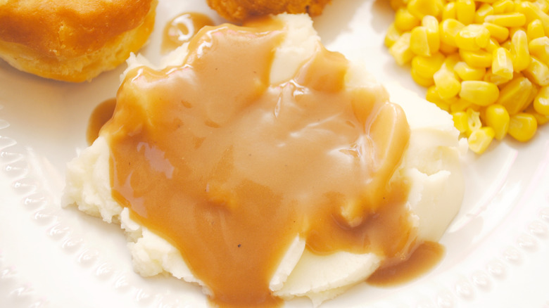 Mashed potatoes and gravy on a plate with corn, biscuits, and fried chicken
