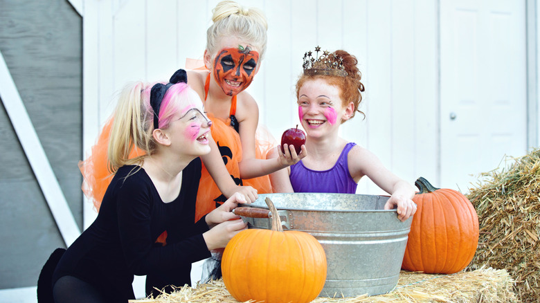 Three children in Halloween costumes bob for apples from a metal bin