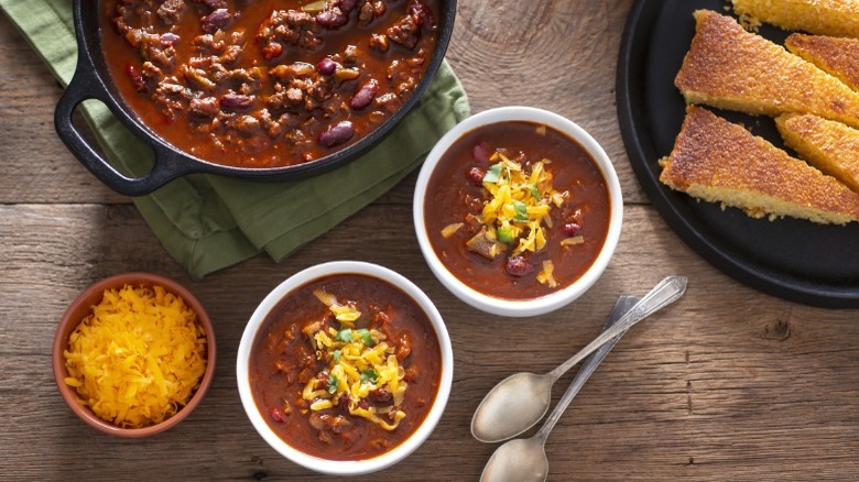 Bowls of chili with cornbread, cilantro, and cheese.